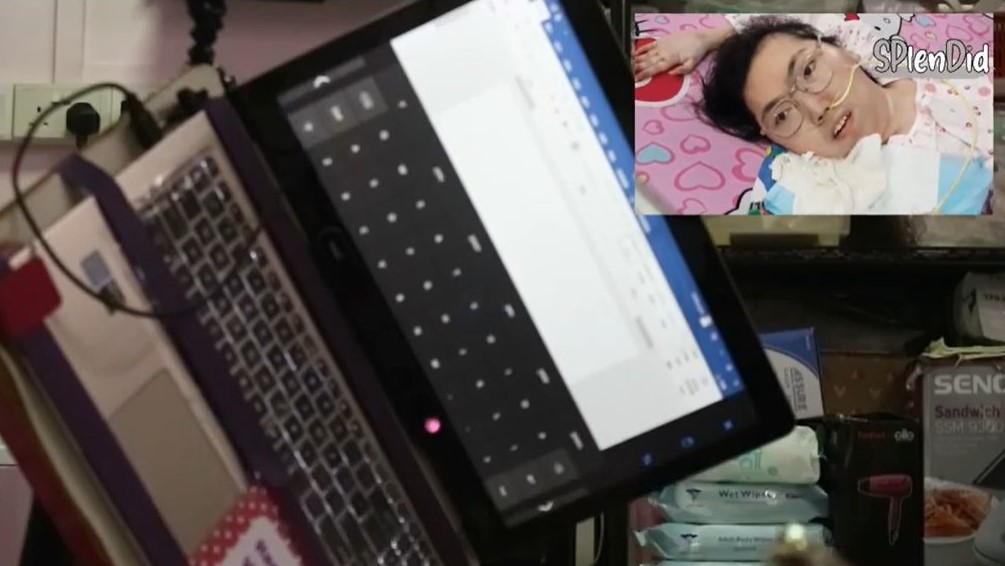 Photo of Vivian showing her on a bed and looking at the direction of her laptop screen on which she tries to type with eye-gaze technology by looking at the alphabets of the on-screen keyboard.
